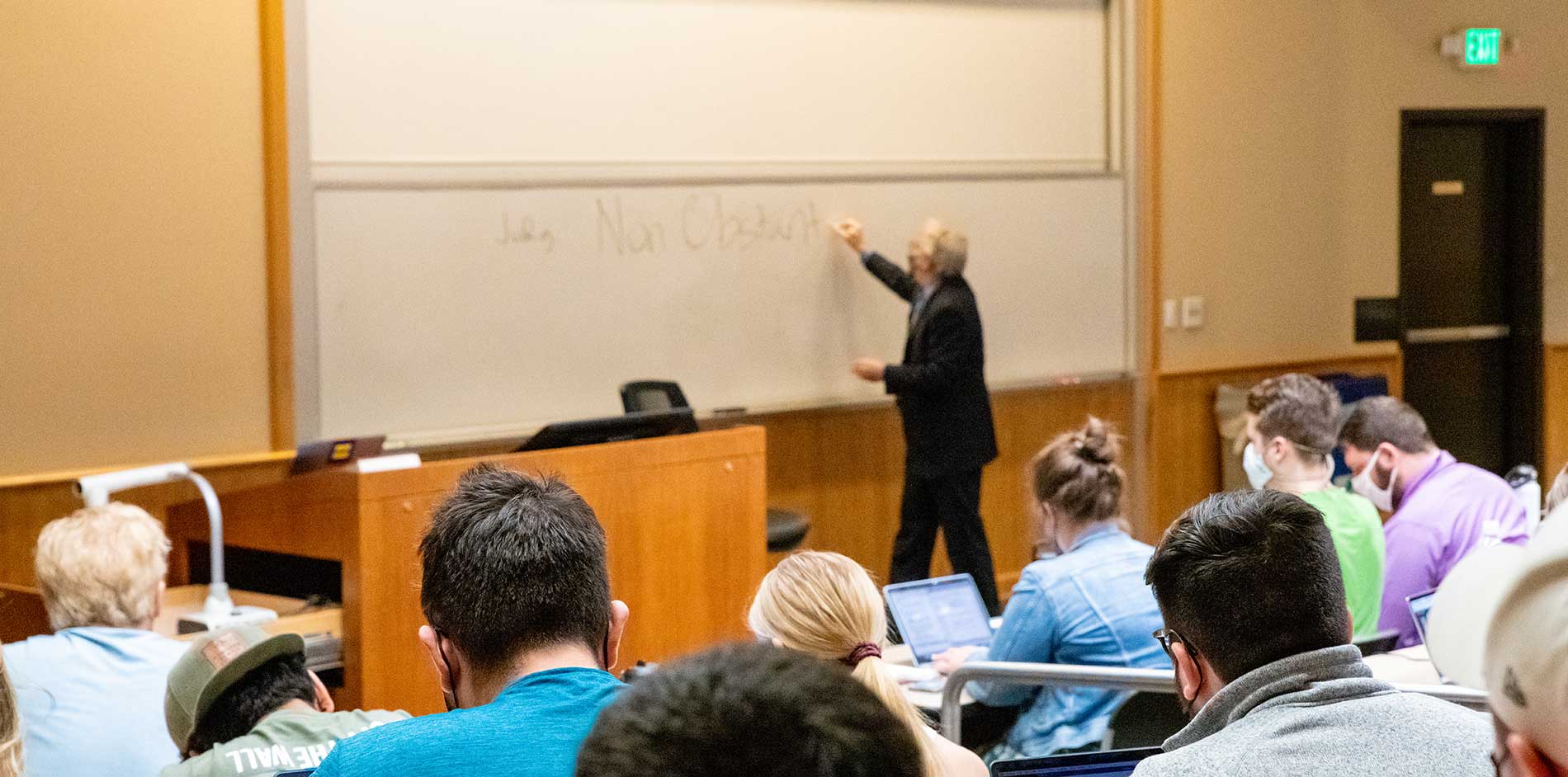 Students in auditorium class with professor writing on white board