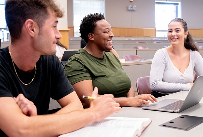 Three students discussing class lecture with laptop and book