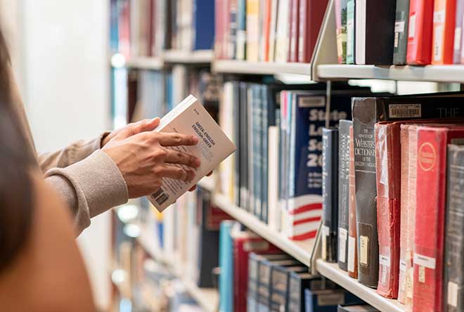 student pulling book from library shelf