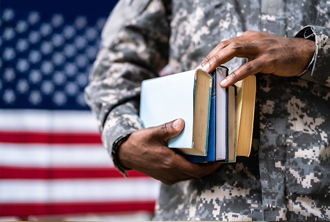 service member in uniform holding a book in front of the American flag