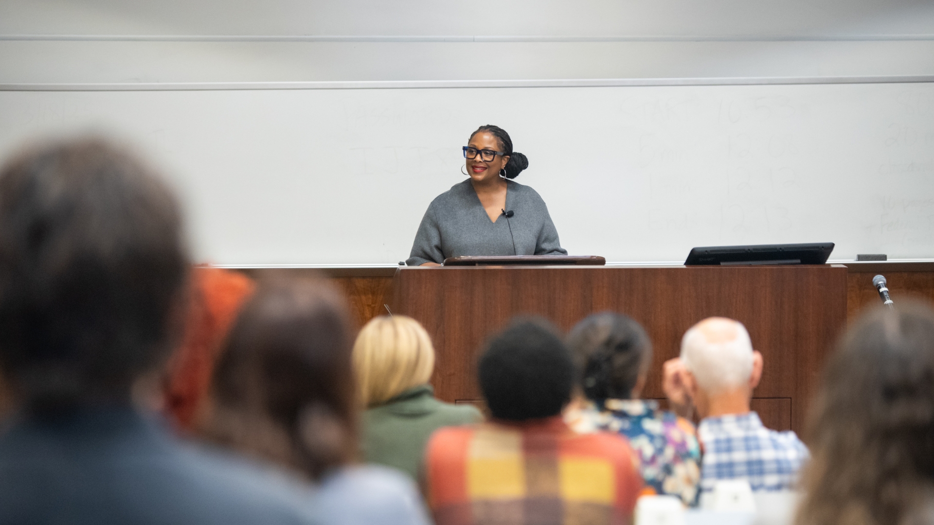 Deborah Archer stands in front of a lecture hall, the backs of her audience fill the foreground.