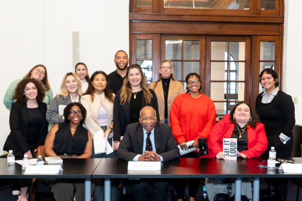 A diverse group of students post behind a seated Randall Kennedy for a group photo. 