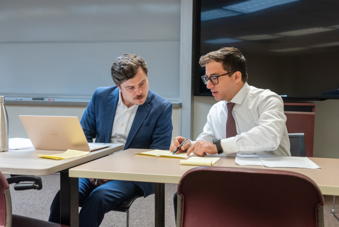 two students discuss their notes while sitting next to each other at a table