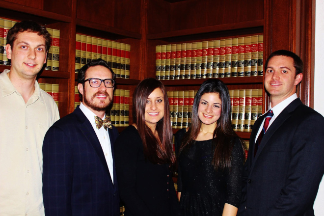 Five students pose in front of books on a bookshelf