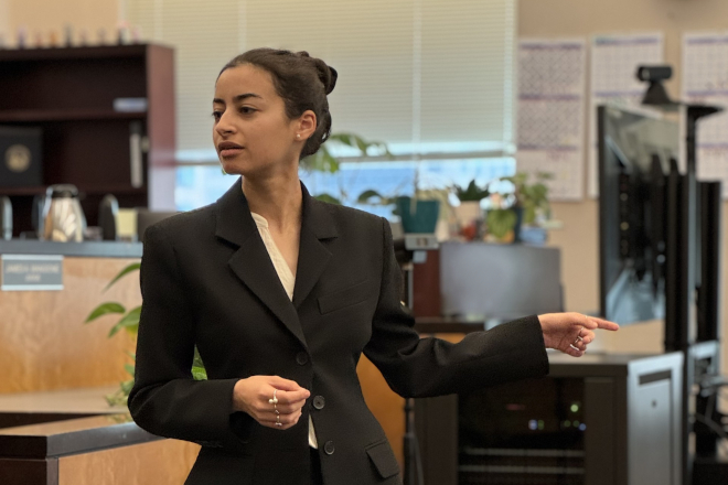 Student stands in front of an office desk and points to their left