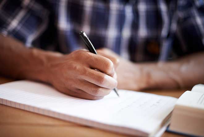 person writing on a notepad with laptop