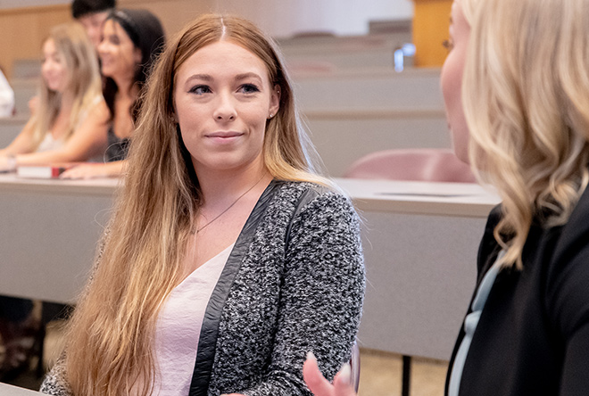 Two female students discussing lecture in auditorium