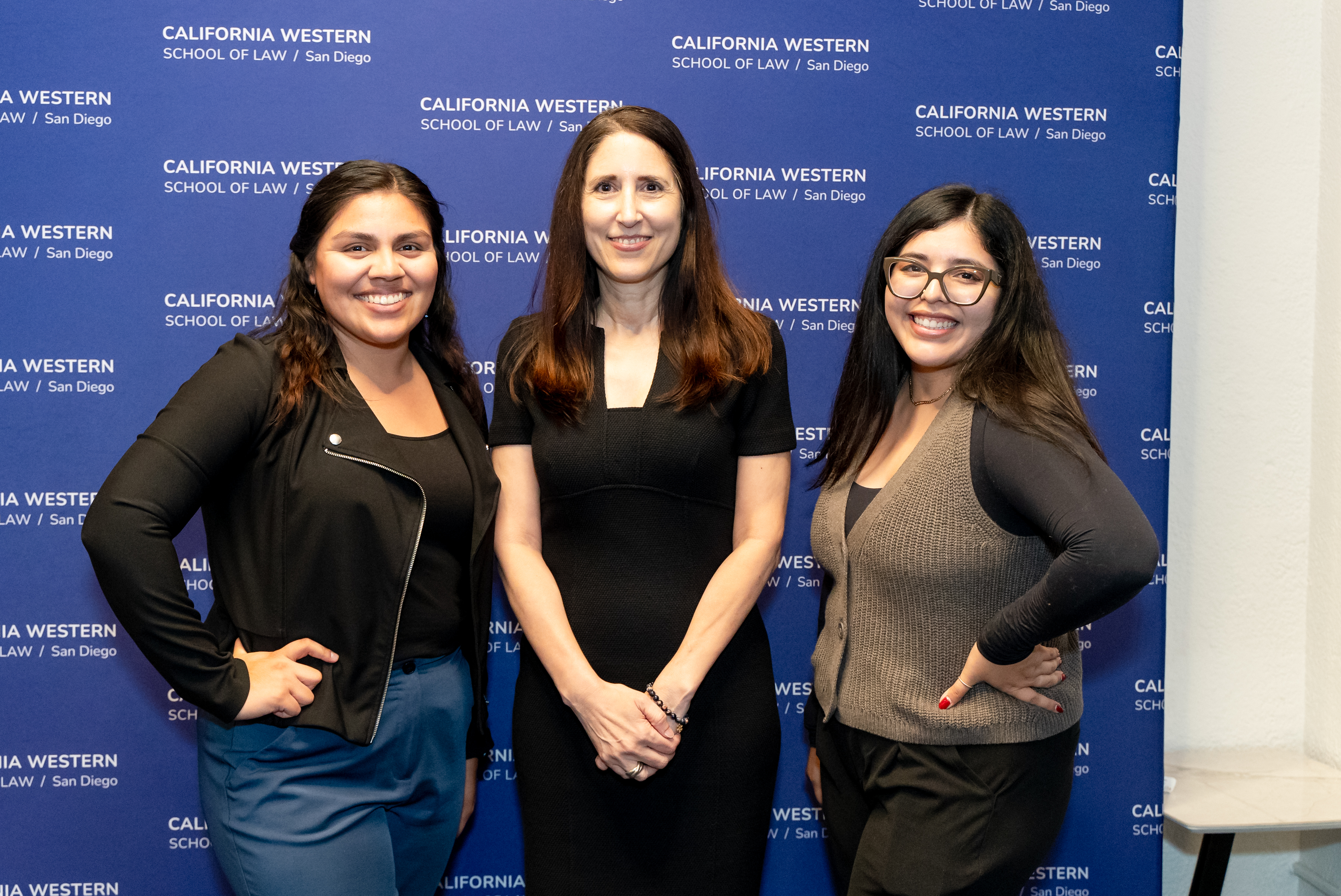 Three women smiling and posing in front of a purple backdrop that reads "California Western School of Law / San Diego.