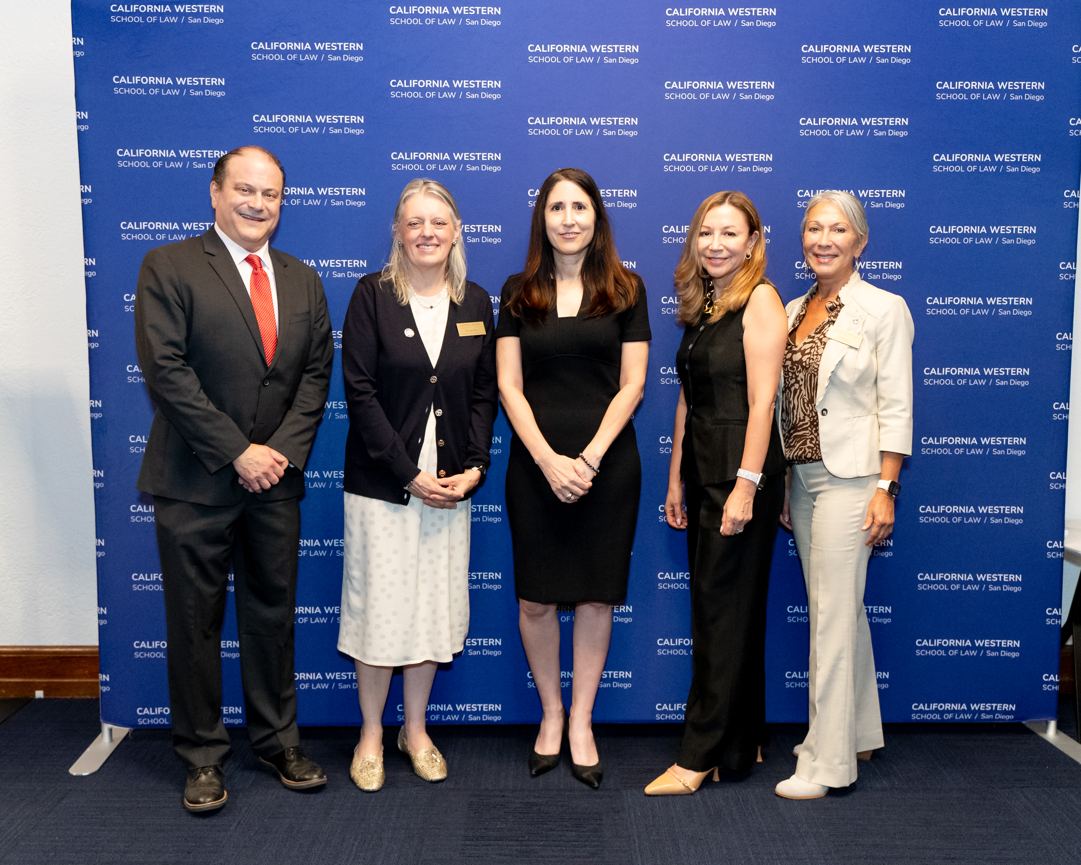 The image shows five individuals standing together for a photo in front of a backdrop with the California Western School of Law logo. The group includes a mix of men and women dressed in professional attire.
