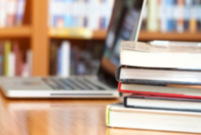 stack of books on table with computer in the background