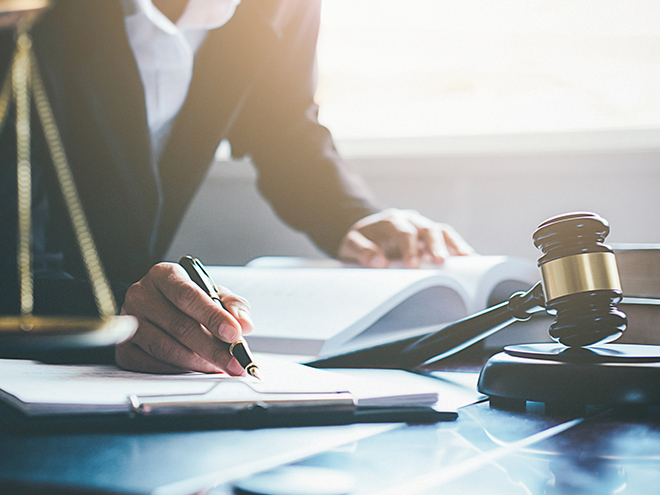 Scale of Justice and gavel with someone writing on desk