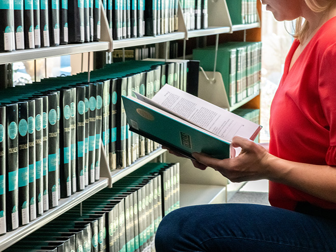 Student reading book near library shelf